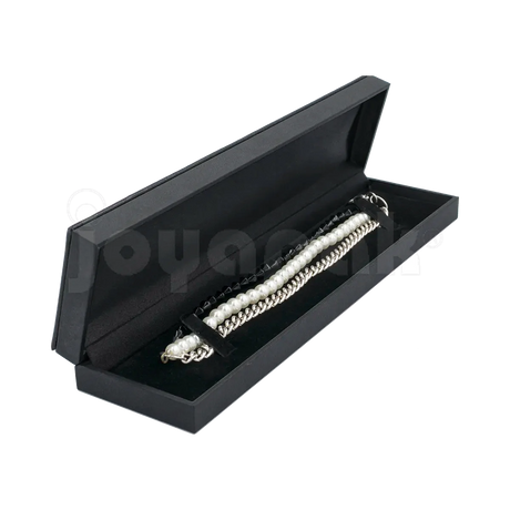 Estuche Italia de color negro con marco interior dorado estrecho para pulsera, caja abierta alargada mostrando una pulsera fina colocada sobre terciopelo blanco.