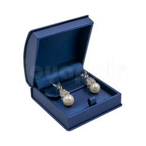 Estuche Zafiro de color azul con listón y moño blanco de formato medio para aretes o dijes, caja abierta mostrando un dije colocado.